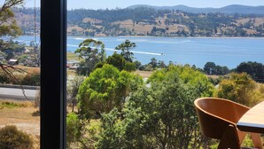 A view through a window of a coastal landscape with a body of water, trees, and distant hills. - The Tamar Ridge Lookout at Tamar Ridge Apartments (Grindelwald)