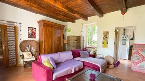 Un accogliente soggiorno con soffitto in legno, un divano rosa, un tavolino da caffè in vetro e una poltrona in vimini.