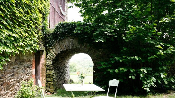Zona salotto all'aperto con arco in pietra, un tavolo e due sedie.