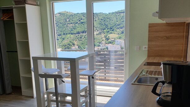 Una cucina moderna con piano di lavoro in legno, lavello e macchina da caffè. C'è un'area pranzo con tavolo e sedie, e vista su un paesaggio verde attraverso una grande finestra.
