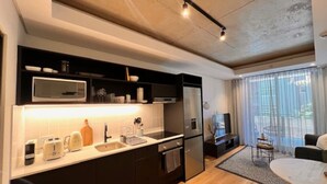 A modern kitchen with a built-in microwave, toaster, and refrigerator. There is a dining area with a table and chairs, and a large window providing natural light. - Lifestyle Apartment at Stationhouse (Cape Town)