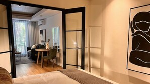 A bedroom with a bed, a desk, and a chair. There is a window with curtains and a view of another room. - Lifestyle Apartment at Stationhouse (Cape Town)