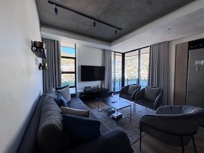 A modern living room with a sofa, armchairs, a coffee table, and a flat-screen TV. - Leisure Apartment at Stationhouse (Cape Town)