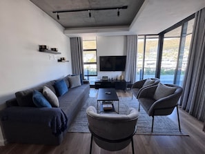 A modern living room with a sofa, two armchairs, a coffee table, and a flat-screen TV. - Leisure Apartment at Stationhouse (Cape Town)