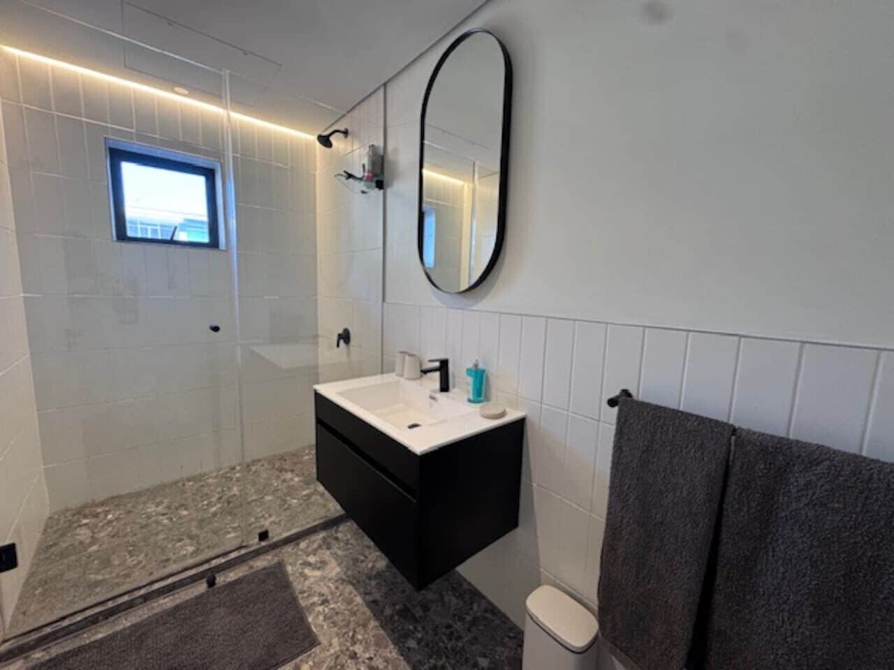 A modern bathroom with a glass-enclosed shower, a black vanity with a white countertop, a large mirror, and a towel rack.