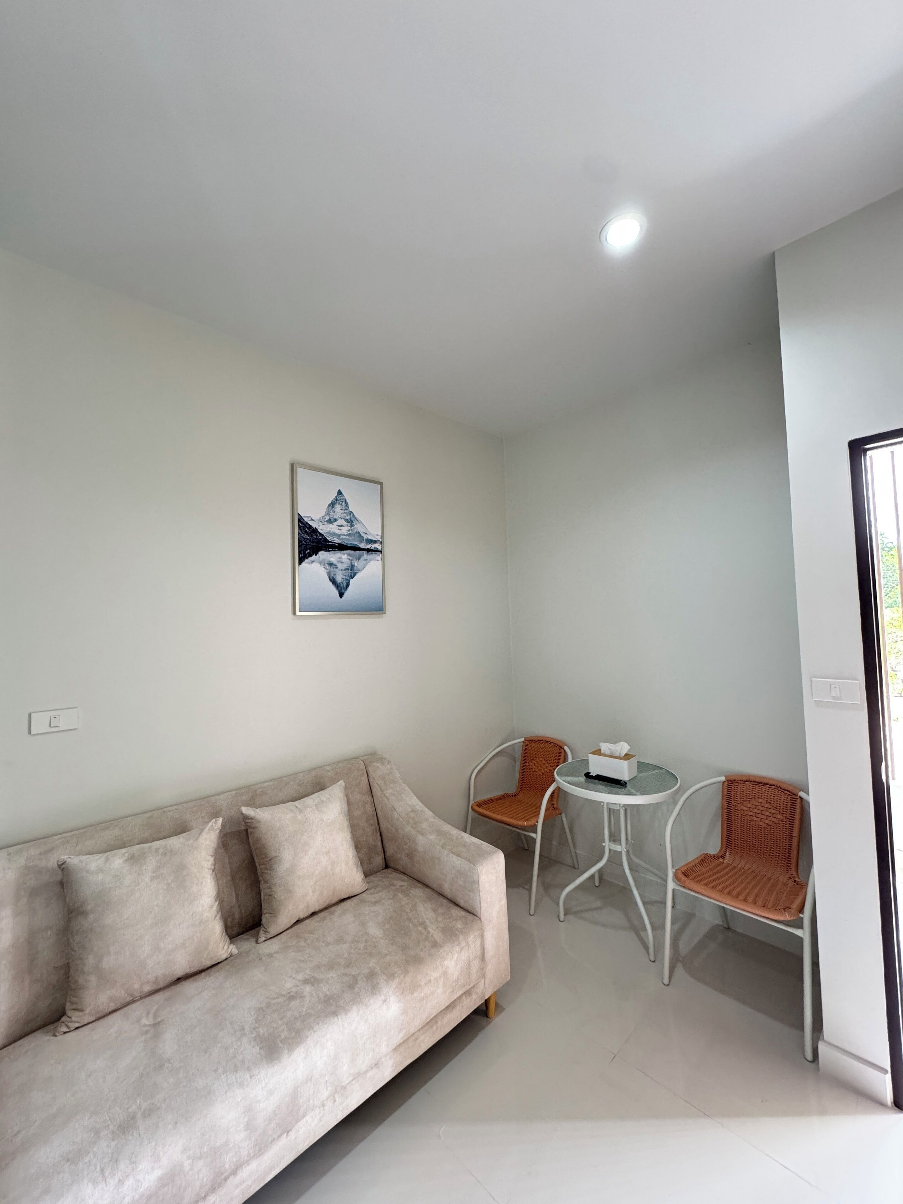 A modern living room with a beige sofa, two wicker chairs, a small round table, and a framed picture on the wall.