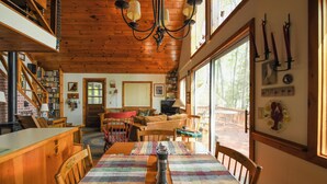 L’intérieur chaleureux d’un chalet comprend un coin repas, un plafond en bois, des étagères et une grande fenêtre.