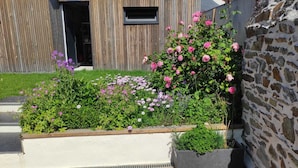 Un jardín con diversas flores y plantas, una cerca de madera y un muro de piedra.
