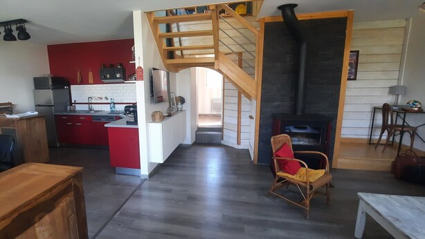 Un espacio habitable amplio con cocina, una mesa de comedor, una escalera de madera y una chimenea.