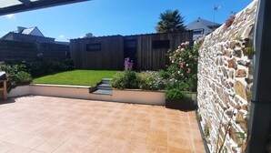 Un patio con piso de baldosas, un banco de madera y un pequeño jardín con flores y plantas.