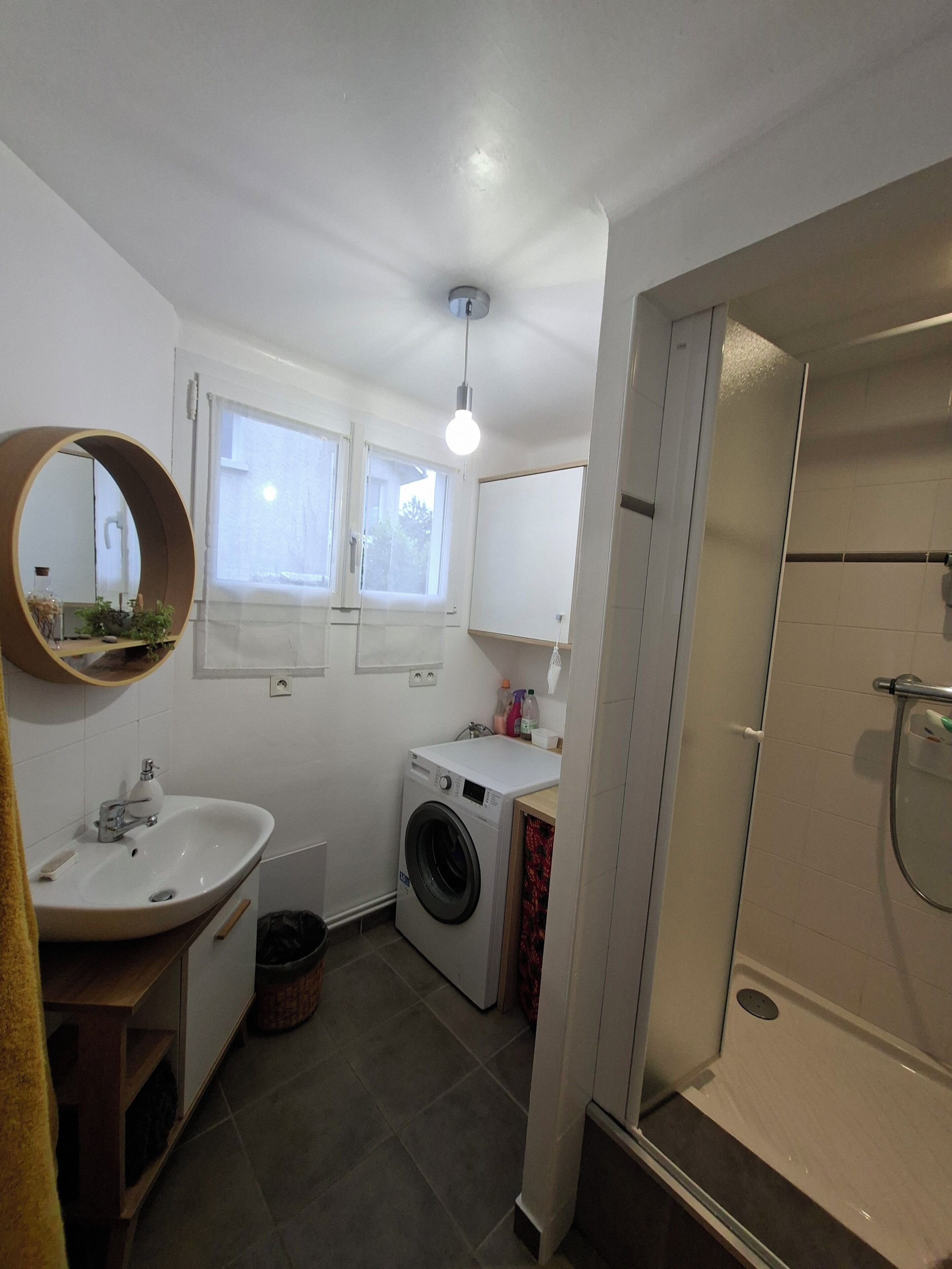 Un baño moderno y compacto con lavamanos, espejo, lavadora y ducha.
