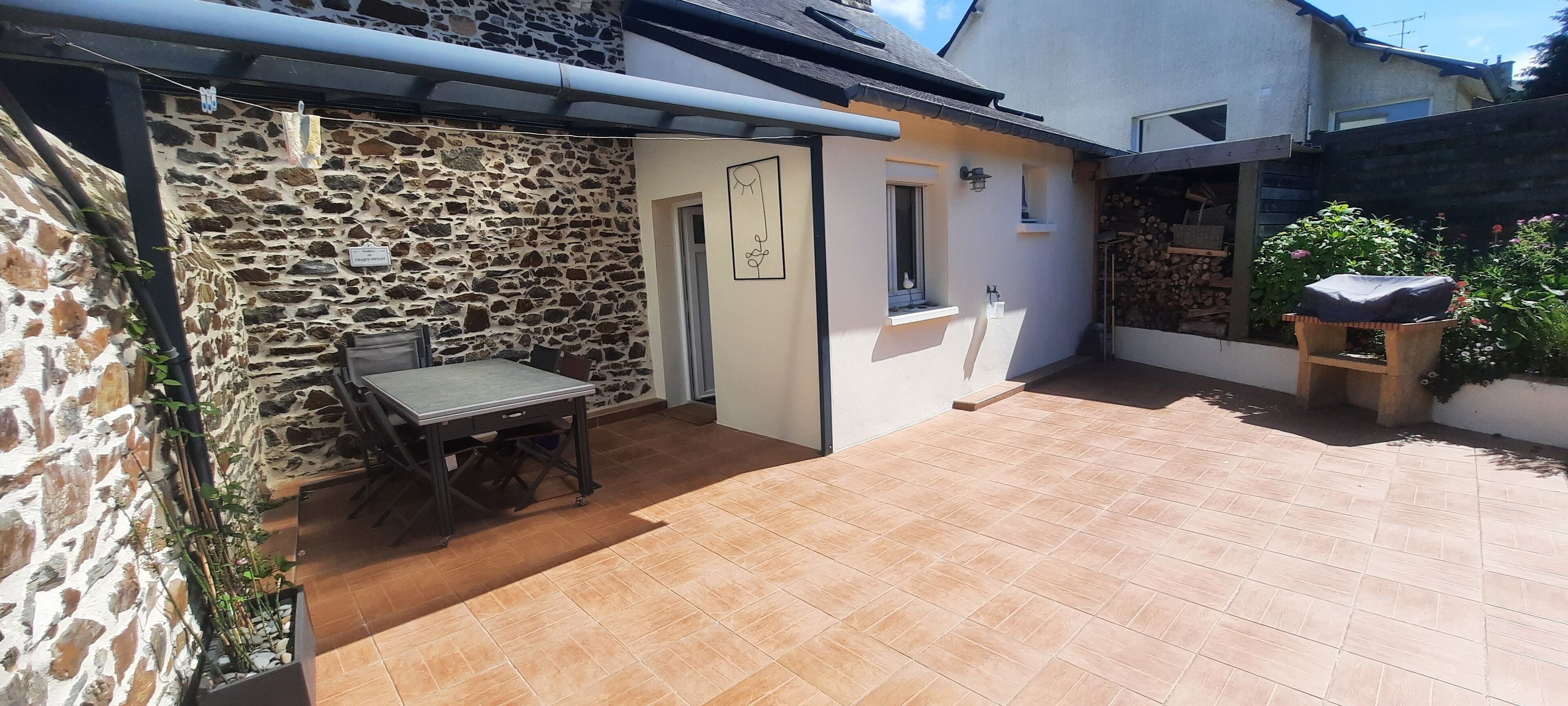 Un muro exterior de piedra, un patio con mesa y sillas, y un pequeño jardín con un banco de madera.