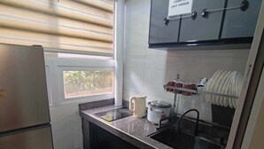 Una cocina compacta equipada con refrigerador, lavaplatos y una ventana con persianas.