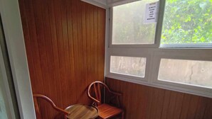 Una habitación pequeña con paneles de madera, una mesa redonda con dos sillas, una cama para mascotas azul y una ventana con un aviso para siempre cerrar y asegurar las ventanas.