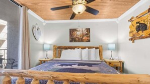 A bedroom with a wooden headboard, a ceiling fan, two bedside tables with lamps, a bed with a patterned bedspread, and a painting on the wall.