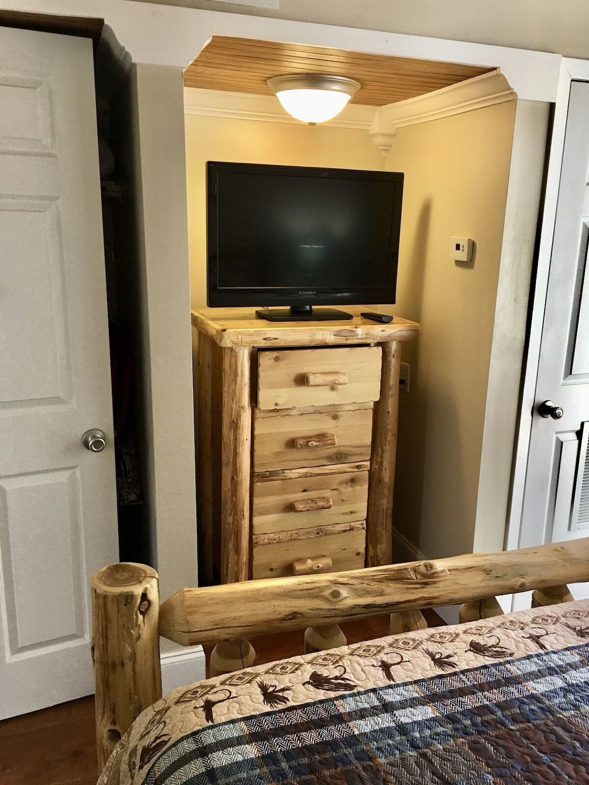 Une chambre avec une commode en bois, un téléviseur posé dessus et un lit recouvert d’une couvre-lit à motifs.