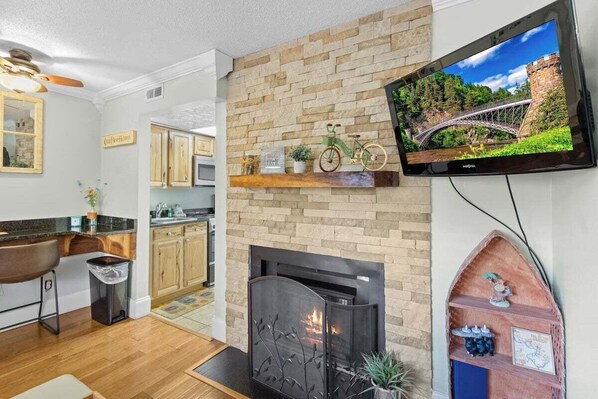 A modern kitchen with a stone backsplash, a fireplace, and a mounted television.
