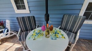 A round table with a floral tablecloth, two striped chairs, and a bottle of wine.