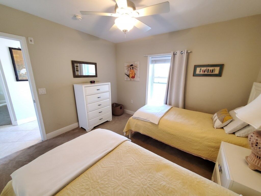 A bedroom with two beds, a ceiling fan, a dresser, and a window with curtains.
