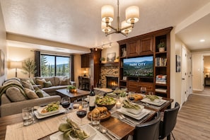 A spacious living room with a fireplace, a dining area set for a meal, and a television displaying 'PARK CITY UTAH'.