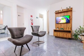 A lobby with two grey upholstered chairs, a wooden entertainment unit with a TV, and a fire extinguisher on the wall. - AFS LOFT HOSTEL ARACAJU (Aracaju)