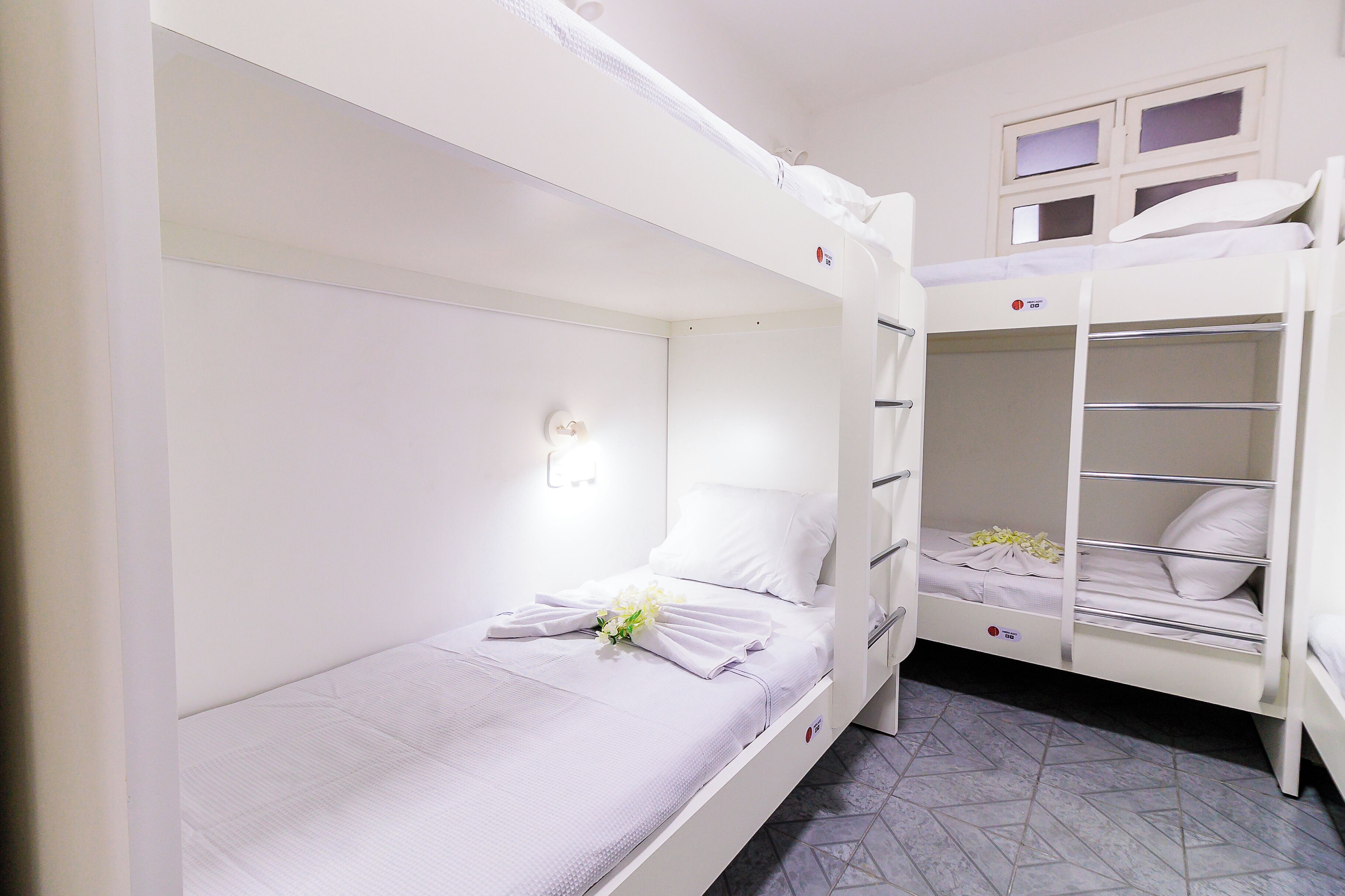 A bunk bed room with a white color scheme, a night light, and a flower on the bed.