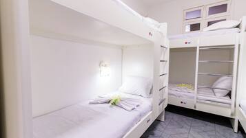 A bunk bed room with a white color scheme, a night light, and a flower on the bed.