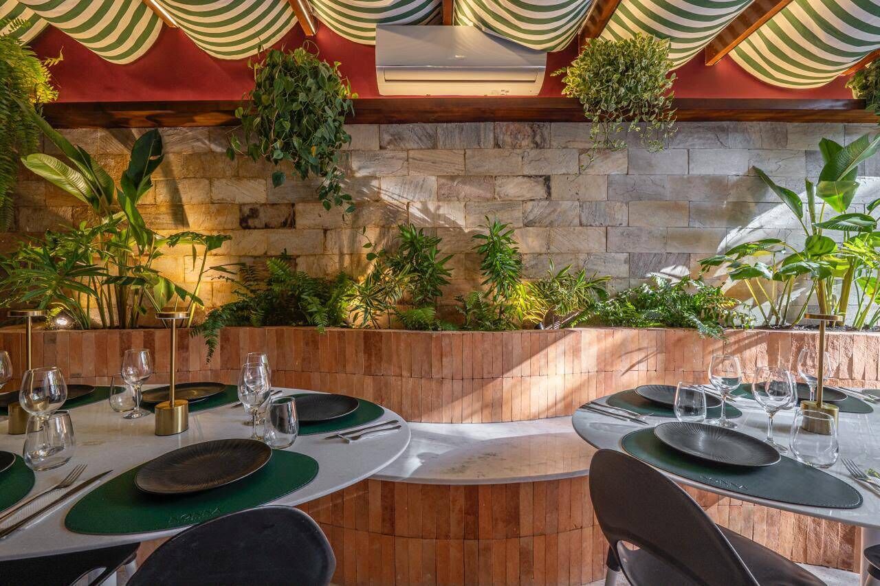 Un espace de restauration en plein air agrémenté de murs en pierre, de plantes vertes et de décorations en tissu à rayures.
