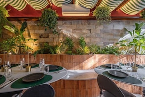 An outdoor dining area with stone walls, green plants, and striped fabric decorations. - AFS LOFT HOSTEL ARACAJU (Aracaju)