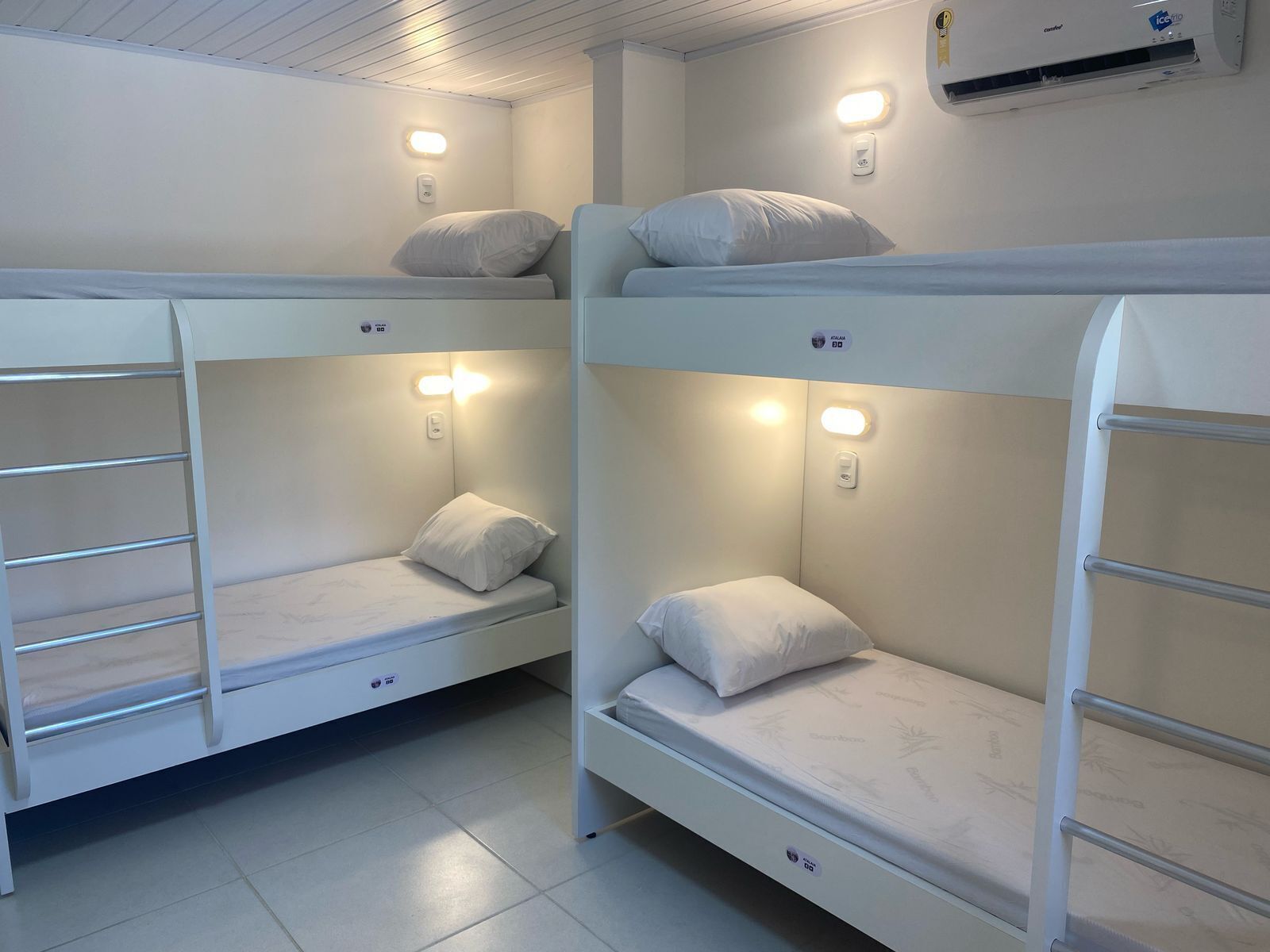 Camas literas con escritorios integrados y espacio de almacenamiento, cada una con mesita de noche y luz de pared.