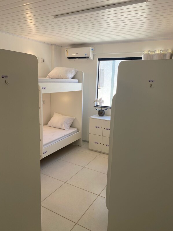 Habitación con literas, una ventana, una mesita con un florero y un armario blanco.