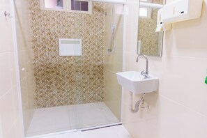 Una doccia a pavimento con rivestimento murale dal motivo geometrico, un lavandino bianco e uno specchio sopra.