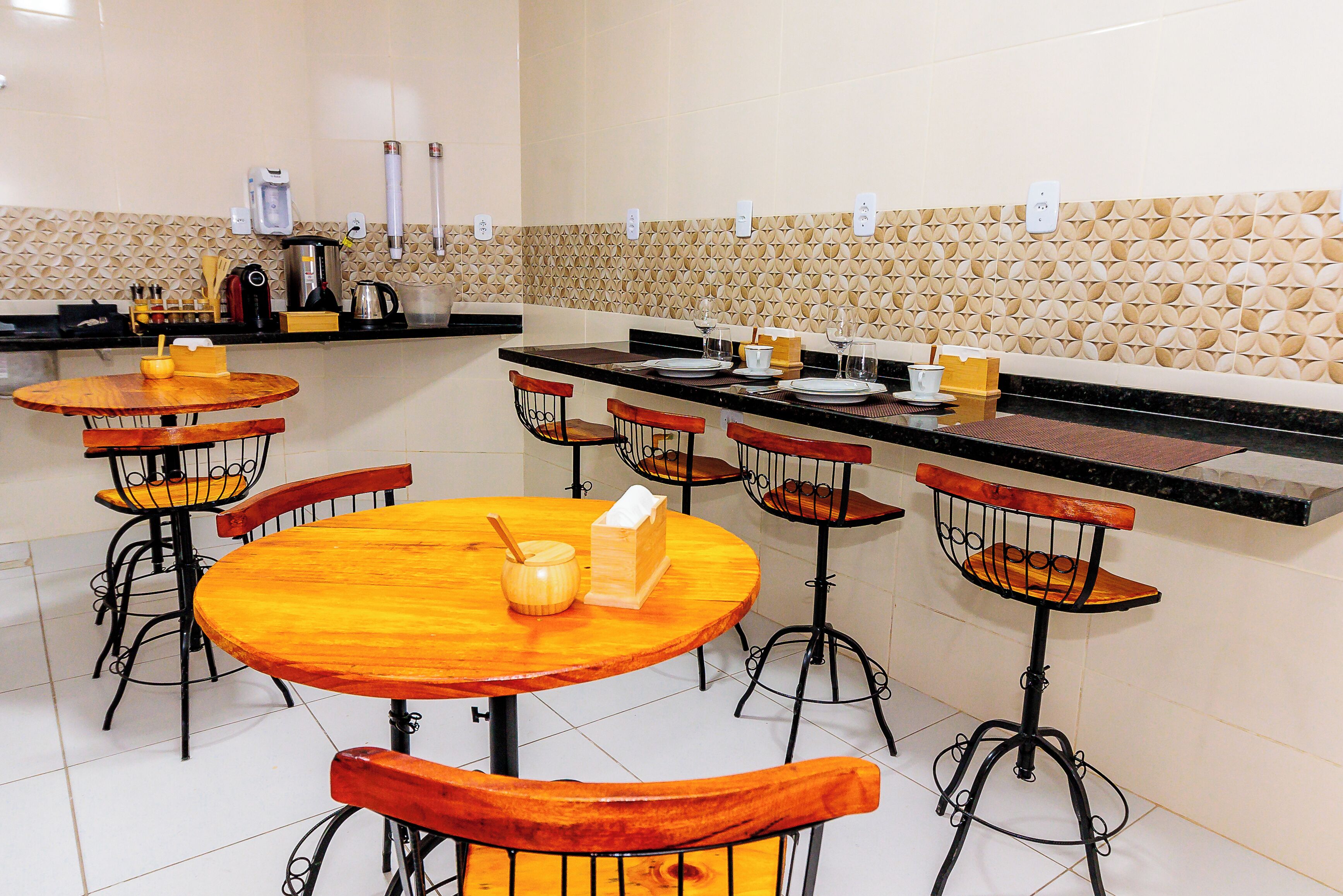 Un restaurante con mesas redondas de madera y sillas de metal, una zona de cocina con electrodomésticos y un salpicadero con diseño.