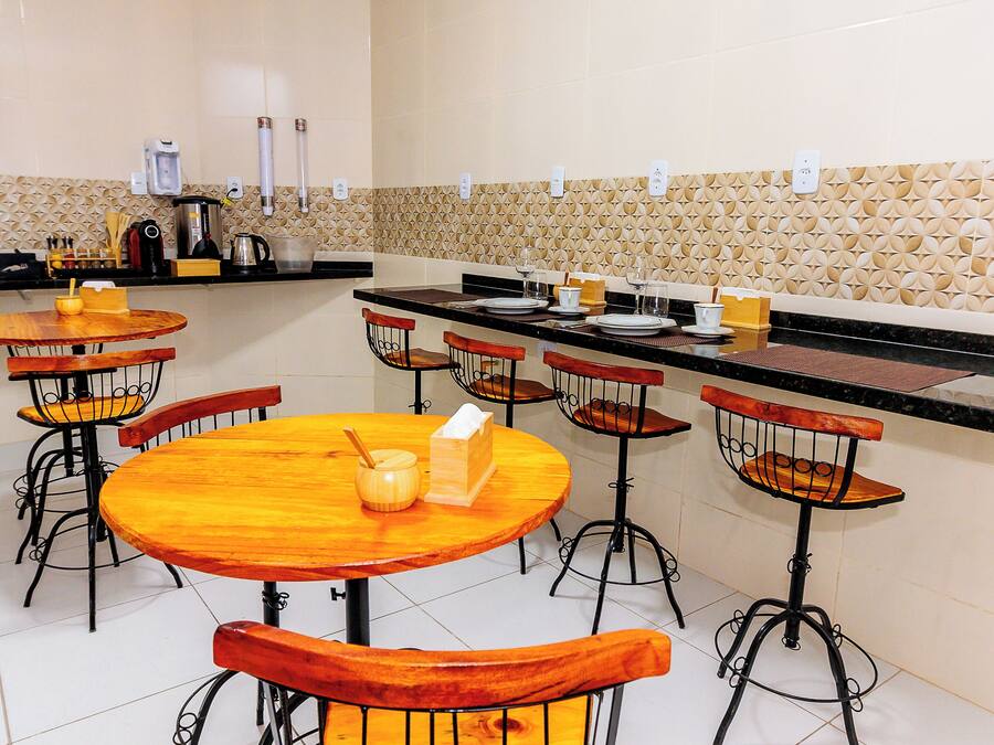 Un restaurante con mesas redondas de madera y sillas de metal, una zona de cocina con electrodomésticos y un salpicadero con diseño.