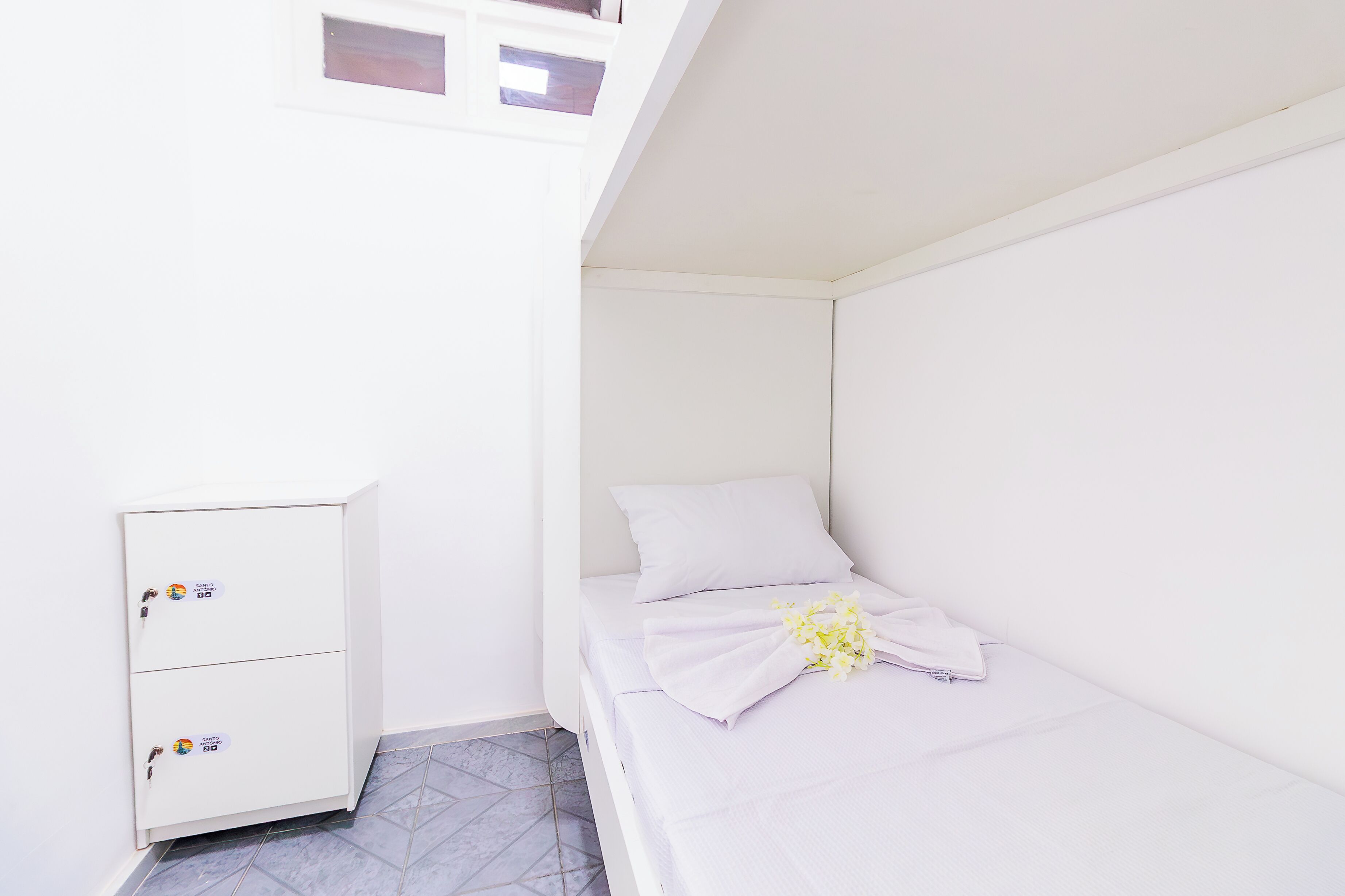 Una habitación pequeña y blanca con una cama, un armario blanco y una ventana.