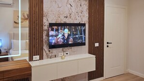 Un dormitorio moderno con una televisión montada en la pared, una cama con cubrecolcha color beige y suelo de madera.