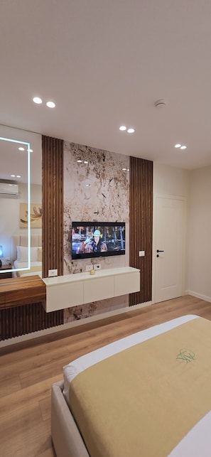 Een moderne slaapkamer met een televisie aan de muur, een bed met een beige deken en een houten vloer.