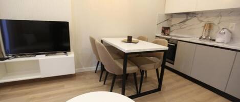 A modern kitchen with a marble backsplash, a dining area with a white table and chairs, and a TV mounted on a white cabinet.