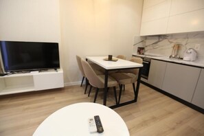 A modern kitchen with a marble backsplash, a dining area with a white table and chairs, and a TV mounted on a white cabinet. - Arkle Apartment 1 (Tirana)