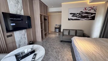Una habitación de hotel moderna con una televisión de pantalla plana, un sofá, una cama, una mesita y un cuadro en la pared.