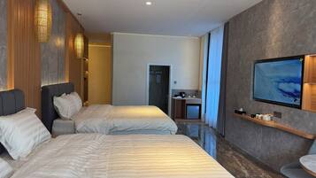 A hotel room with two beds, a TV, a small kitchenette, and a bathroom.