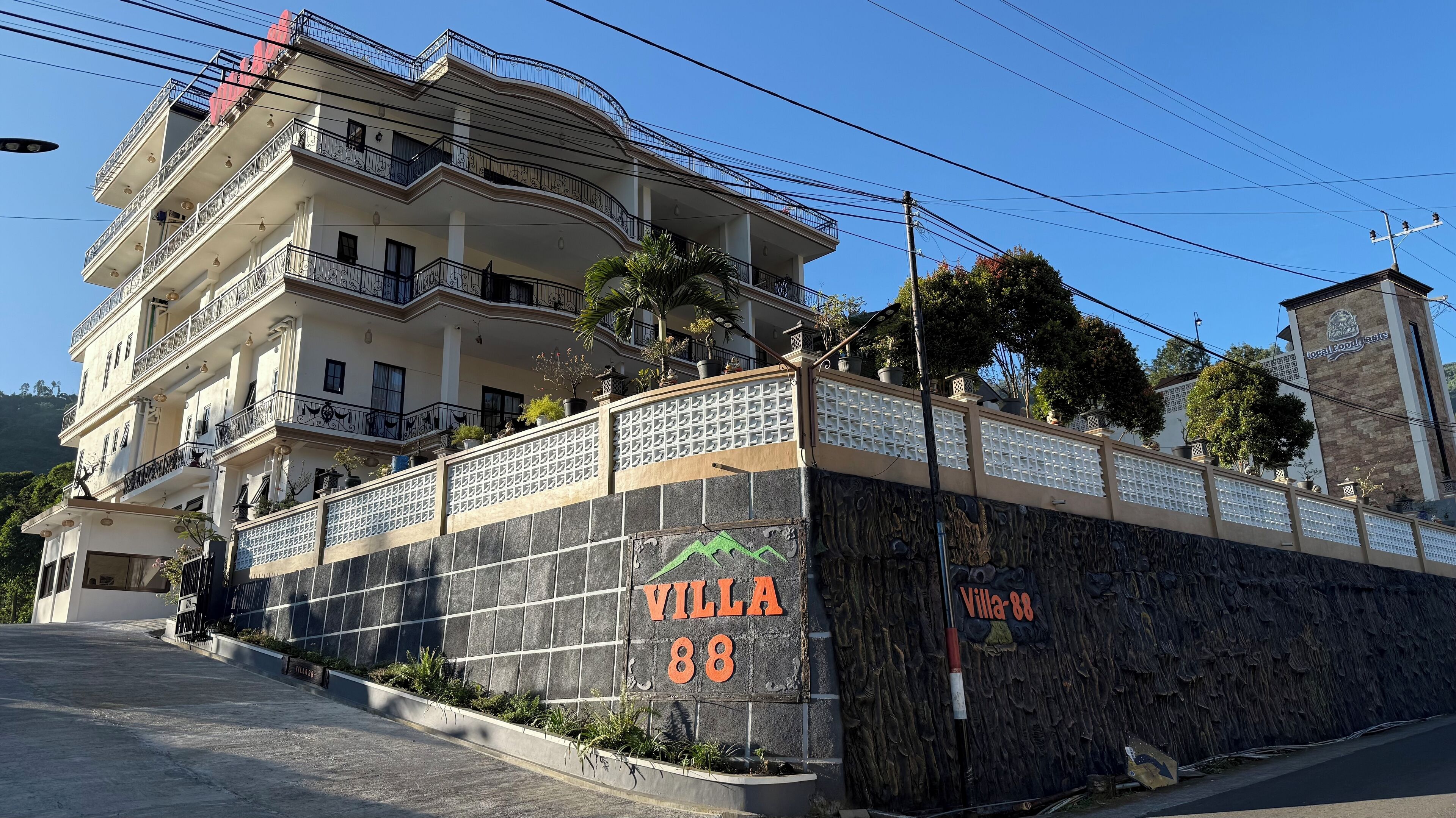 A multi-story building with balconies, a stone wall with the name "Villa 88," and a sign for "Local Food Taste."