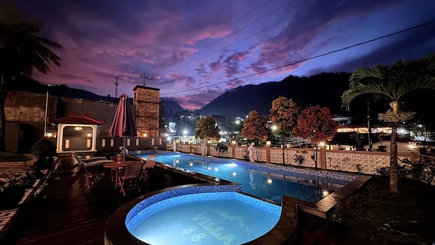 Zona de piscina con un jacuzzi, mobiliario exterior y vistas a la montaña al anochecer.