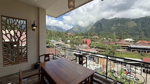Un balcón con una mesa y sillas de madera, con vistas a un paisaje montañoso que incluye edificios y una carretera.