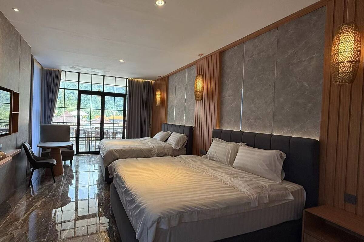 A modern hotel room with two beds, a desk, and a large window offering a view of the outdoors.