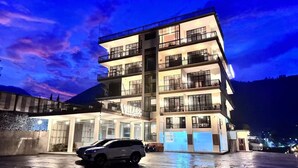 Un hotel de varios pisos con balcones y un coche estacionado frente a él.