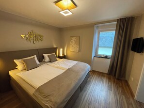 Une chambre d’hôtel avec un grand lit, une table de chevet avec une lampe, une fenêtre avec des rideaux et une œuvre d’art murale.
