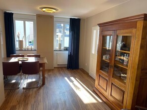 Une pièce comprenant une table à manger en bois, des chaises, un buffet aux portes vitrées et une fenêtre avec des rideaux.