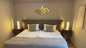 Ein modernes Schlafzimmer mit einem großen Bett, zwei Nachttischen mit Lampen, einer geometrischen Wanddekoration und einem gerahmten Kunstwerk an der Wand.