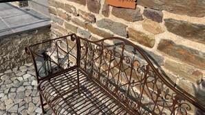 Eine schmiedeeiserne Bank mit Metallgestell und aufwendigen Rankenverzierungen, vor einer Steinmauer mit dem Schild 'Lieblingplatz'.